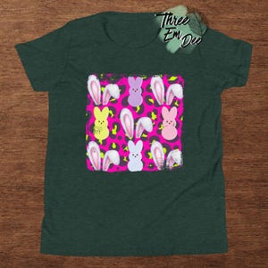 May include: A green t-shirt with a pink and yellow print of pastel-colored Easter eggs with bunny ears on a leopard print background. The text "Three Em Dee" is visible in the top right corner of the image.