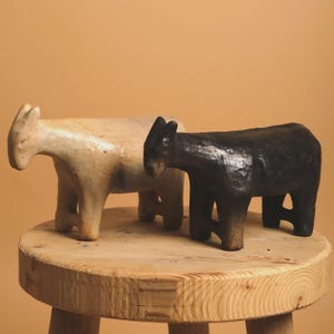 Peut inclure: Deux figurines d'animaux, l'une avec une finition beige clair et l'autre avec une finition noire foncée, présentant toutes deux une surface lisse et texturée avec des oreilles pointues et quatre pattes robustes, côte à côte.