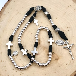 Può includere: Un rosario nero e argento con perline e croci argentate. Il rosario ha un ciondolo d'argento della Vergine Maria e un crocifisso d'argento.