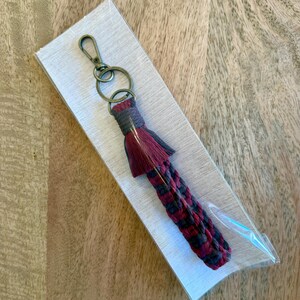 Puede incluir: Un llavero trenzado de color burdeos y negro con un borla y un anillo de llave plateado.
