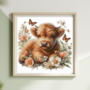 May include: A framed print featuring a Highland calf lying amidst flowers and butterflies. The calf has brown fur and small horns. The flowers are peach and white, and the butterflies are orange. The artwork is in a wooden frame.