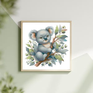 May include: A framed watercolor print of a koala bear sitting on a tree branch. The koala is light gray with fluffy ears and a small black nose. The tree has green leaves and small green berries. The frame is a light wood color.