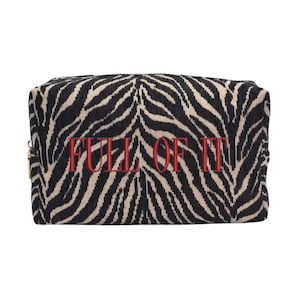 May include: A rectangular cosmetic bag with a zebra print pattern in black and beige. The words "FULL OF IT" are embroidered in red across the center. The bag has a gold zipper.