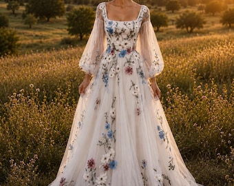 May include: A floor-length gown featuring a square neckline and sheer, long bishop sleeves. The dress is made of white fabric adorned with embroidered floral patterns in shades of blue, pink, and white, cascading from the bodice to the hem.