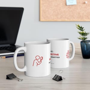 May include: Two white ceramic mugs with red graphics and text. One mug features a person with a magnifying glass, the other has text that reads "BE EFFECTIVE, BE COMMITTED, BE IN A WAY that inspires you". A ladybug graphic is also on the second mug.