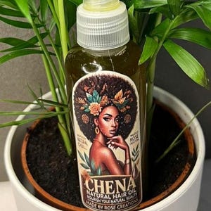 May include: A clear glass bottle with a yellow cap and a label that says "CHENA NATURAL HAIR OIL NOURISH YOUR NATURAL BEAUTY MADE BY ROSE CREATIONS". The bottle is sitting in a white pot with green plants.