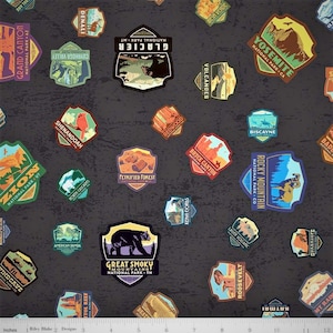 May include: A dark gray fabric featuring a repeating pattern of colorful national park-themed patches. The patches display various park names and illustrations, including Yosemite, Glacier, and Rocky Mountain. The fabric has a textured appearance.