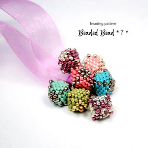 以下が含まれることがあります： ピンク、ティール、グリーン、パープルなど、さまざまな色のビーズビーズのコレクション。シルバーのアクセントが付いています。ビーズは白い表面にピンクのリボンで配置されています。テキストは「beading pattern Beaded Bead *7*」と書かれています。