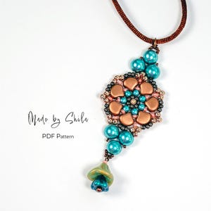 Op de afbeelding: Een handgemaakte hangerketting met een bruin koord. De hanger heeft een bloemmotief met turquoise kralen, koperkleurige elementen en kleine zwarte en roze kralen. De tekst "Made by Shila" en "PDF Pattern" zijn zichtbaar.