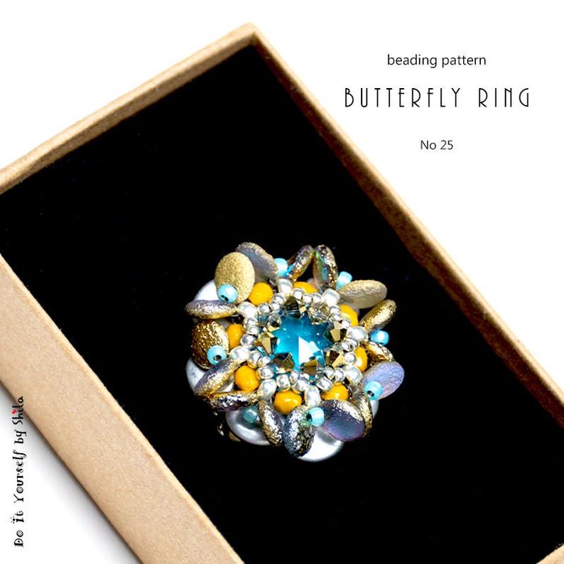 Puede incluir: Un anillo de mariposa con cuentas con una gran gema azul cuadrada en el centro. El anillo presenta cuentas doradas, amarillas e iridiscentes, sobre un fondo negro dentro de una caja de cart&oacute;n. El texto en la imagen dice "beading pattern BUTTERFLY RING No 25".