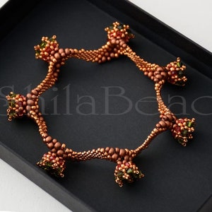 K&ouml;nnte beinhalten: Ein kupferfarbenes Perlenarmband mit einem einzigartigen, offenen Design. Das Armband verf&uuml;gt &uuml;ber eine Reihe von Perlenclustern in Rot-, Gr&uuml;n- und Kupfert&ouml;nen, die ein strukturiertes und verziertes Aussehen erzeugen. Das Armband wird in einer schwarzen Box pr&auml;sentiert.
