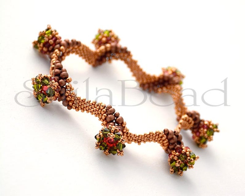 K&ouml;nnte beinhalten: Nahaufnahme von zwei Armb&auml;ndern aus Perlen. Die Armb&auml;nder sind kupferfarben mit Clustern aus gr&uuml;nen, roten und braunen Perlen. Die Armb&auml;nder befinden sich auf wei&szlig;em Hintergrund. Die Armb&auml;nder sind handgefertigt.