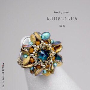 Puede incluir: Un anillo de mariposa con cuentas con una piedra preciosa central de color turquesa, rodeada de cuentas doradas, plateadas y turquesas. El anillo est&aacute; sobre una superficie blanca, con el texto "Butterfly Ring" y "No 25".