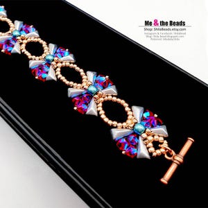 以下が含まれることがあります： 銅製のトグル留め具が付いたビーズブレスレット。ブレスレットは、白、金、虹色の青と赤のビーズの繰り返しパターンを特徴としています。