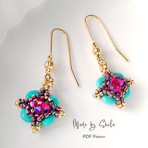 May include: A pair of handmade earrings with a floral design. The earrings feature turquoise beads, a central cluster of pink and purple crystals, and gold-colored metal accents. The text "Made by Shila" and "PDF Pattern" are visible.