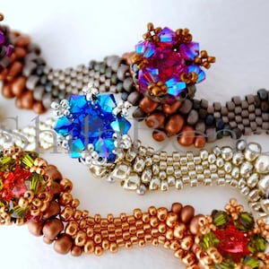 K&ouml;nnte beinhalten: Nahaufnahme von Perlenschmuck mit aufwendigen Designs. Die St&uuml;cke zeigen eine Vielzahl von Farben, darunter Blau, Rot, Gr&uuml;n und Gold, mit Fokus auf die detaillierte Perlenarbeit und funkelnde Akzente. Der Schmuck scheint handgefertigt zu sein.