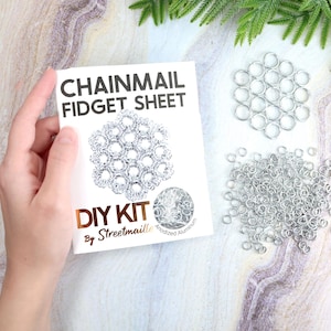 May include: A DIY chainmail fidget sheet kit is shown. The kit includes a white card with the text "CHAINMAIL FIDGET SHEET" and "DIY KIT". Loose silver metal rings and a completed sheet are also visible.