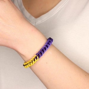 Stretchy chain bracelet made from black metal rings, half yellow rubber rings and half purple rubber rings on a models wrist.