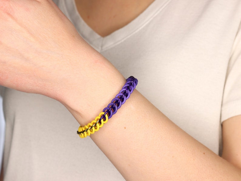 Stretchy chain bracelet made from black metal rings, half yellow rubber rings and half purple rubber rings on a models wrist.