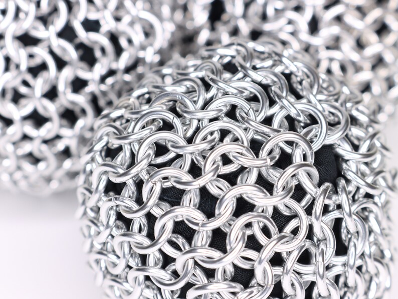 A very close up example of a finished silver chainmail ball against a white background.