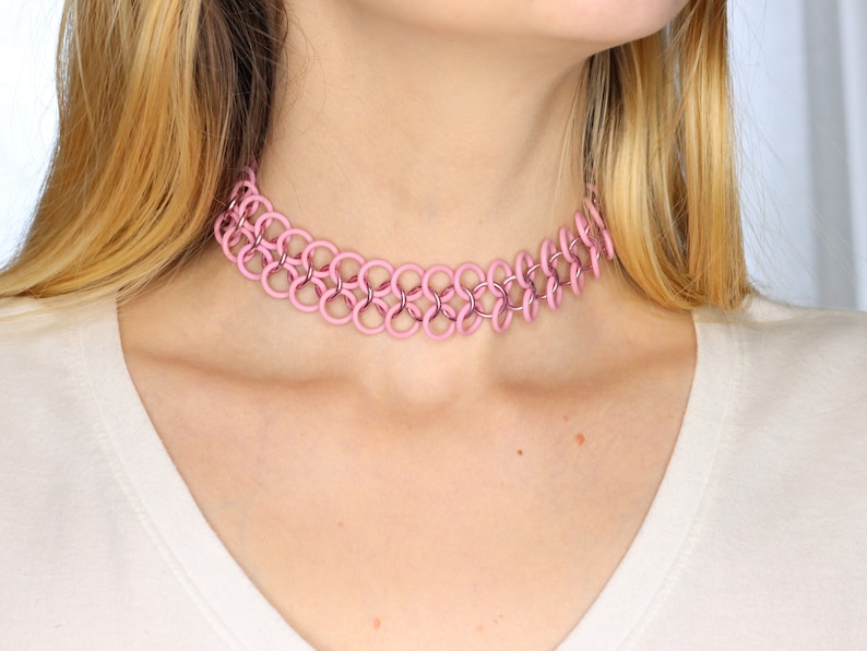 A pink oversized tattoo choker made with pink rubber rings connected by shiny pink metal rings in a chainmail pattern.