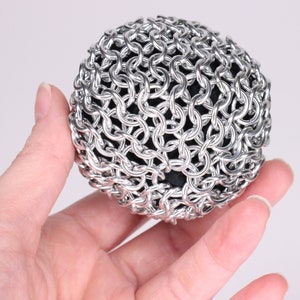 A close up example of a finished chainmail ball made held in a hand at another angle to show the metal fabric texture.