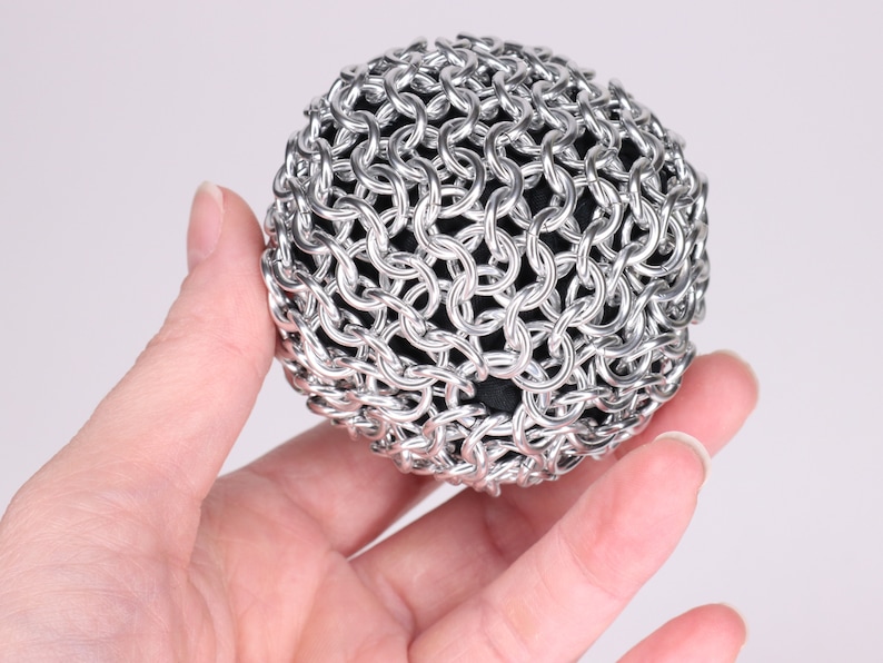A close up example of a finished chainmail ball made held in a hand at another angle to show the metal fabric texture.