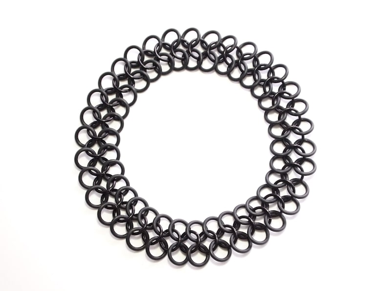 An oversized chainmail tattoo choker laying in a flat circle on a white table. The full choker is visible, showing the seamless design without a clasp.