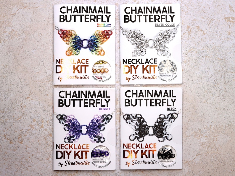 A photo of four of the butterfly kit colors including: Rainbow, starting with red on the wingtips and moving through the rainbow to purple in the center. Silver, a simple silver anodized aluminum butterfly. Purple, a mostly purple butterfly with lighter purple and black wing tips with white spots. Black, a mostly black butterfly with speckled white wingtips.