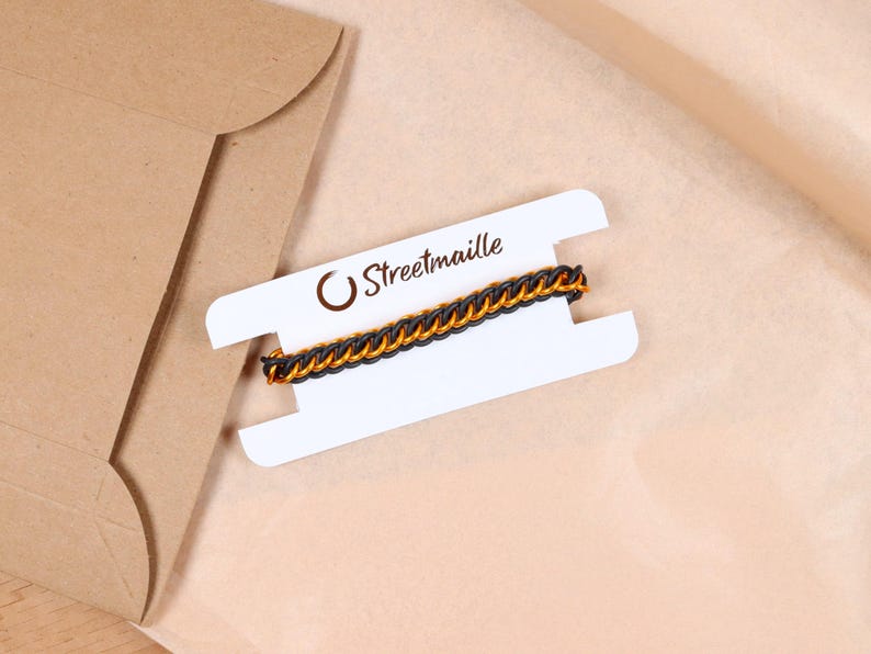 A custom stretchy chain bracelet sitting on top of the paper packaging it comes wrapped in. The bracelet is wrapped around a white paper card to keep it untangled during shipping. The Streetmaille logo is printed on the top of the card in a copper colored foil. The white bracelet card is highlighted by its contrast against the brown wrapping paper and mailer.