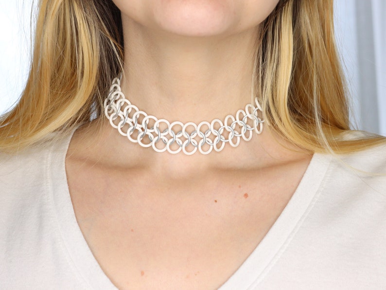 A white oversized tattoo choker made with white rubber rings connected by matte white metal rings in a chainmail pattern.