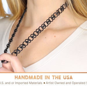 A black oversized tattoo choker being stretched over twice its length away from the models neck with one hand. This necklace is handmade in the USA from US and or imported materials in an artist owned and operated shop.