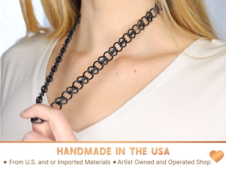 A black oversized tattoo choker being stretched over twice its length away from the models neck with one hand. This necklace is handmade in the USA from US and or imported materials in an artist owned and operated shop.