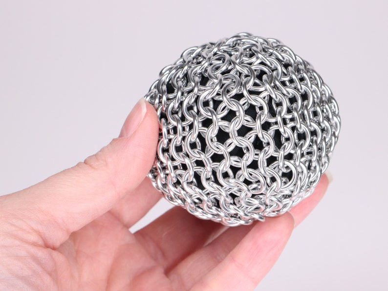 A close up example of a finished chainmail ball made held in a hand to show the metal fabric texture.
