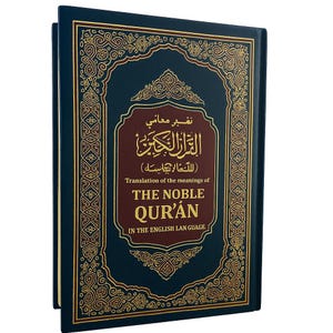 May include: A hardcover book with a dark blue cover and gold ornate detailing. The title "THE NOBLE QUR'AN" is displayed in gold lettering, with Arabic script above. The book's spine is also dark blue.