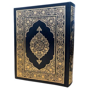 May include: A hardcover book with a black cover and gold ornate designs. The cover features a central medallion with Arabic script and intricate patterns. The edges of the book are also gold. The book is standing upright.
