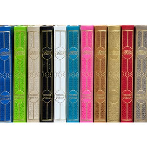 May include: A collection of colorful, hardcover copies of The Noble Qur'an. The spines are in various colors, including blue, green, black, white, teal, pink, gold, red, and gray. Each book has gold lettering and decorative accents.