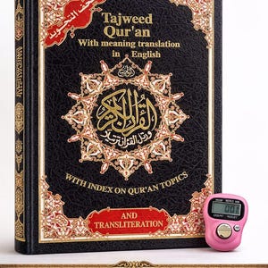 May include: A black Tajweed Qur'an with gold and red detailing, featuring English translation and index on Qur'an topics. Includes a pink digital counter. The book's cover displays ornate Arabic calligraphy and text. The title is "Quran + Free Tasbeeh Gift".