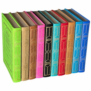 May include: A collection of ten hardcover books titled The Noble Qur'an, arranged in a row. Each book features a distinct solid color cover including lime green, gold, brown, pink, black, turquoise, red, tan, light blue, and royal blue.