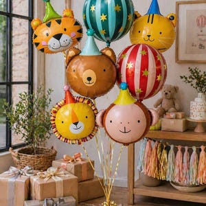 May include: A collection of animal-shaped foil balloons, including a tiger, bear, lion, and monkey, each wearing a party hat. Other balloons feature striped and star patterns. The balloons are tied together with gold ribbons, perfect for a birthday party.