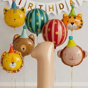 May include: A collection of foil balloons featuring a large beige number one, animal faces including a lion, bear, tiger, and monkey wearing party hats, and two round balloons with star patterns. A white banner reads HAPPY BIRTHDAY in gold letters.