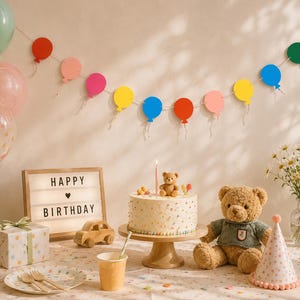 May include: A festive birthday scene with a cake, balloons, and decorations. A cake with a candle and a teddy bear topper sits on a wooden stand. A sign reads "HAPPY BIRTHDAY". A plush teddy bear and party hat are also present.