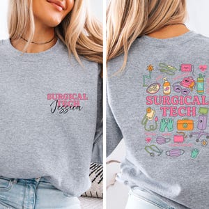 May include: A heather gray sweatshirt with the text "SURGICAL TECH Jessica" in pink and black on the front. The back features a colorful graphic of surgical tools and the words "SURGICAL TECH" in pink.
