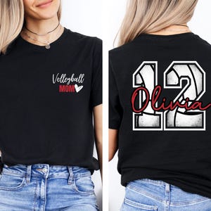 May include: Black t-shirt with a white volleyball design and the text "Volleyball Mom" with a red heart on the front. The back of the shirt has a white volleyball design with the number "12" and the name "Olivia" in red.