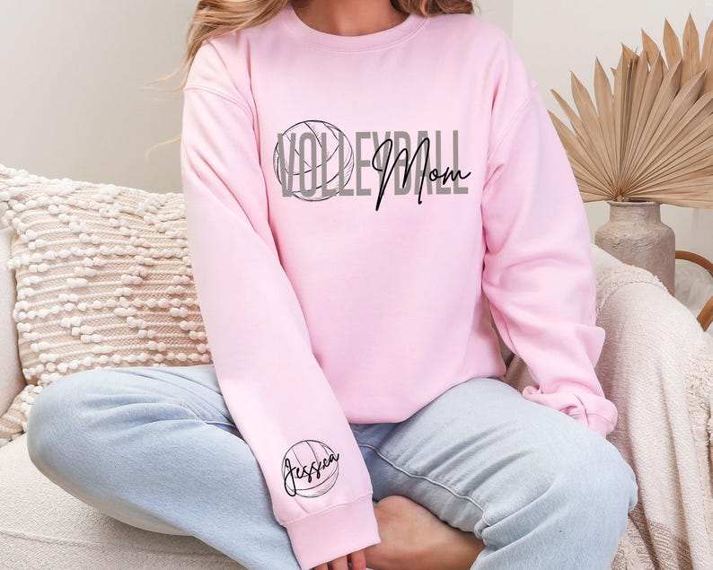May include: A light pink sweatshirt with the words "Volleyball Mom" in gray and black. A volleyball graphic is above the word "Volleyball". The name "Jessica" is printed on the left sleeve, inside a volleyball graphic.