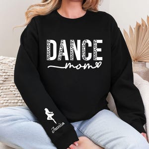 May include: Black sweatshirt with the text "DANCE mom" in white with a leopard print pattern. The sweatshirt has a white silhouette of a dancer on the sleeve with the name "Jessica" underneath.