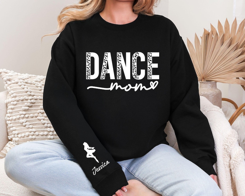 May include: Black sweatshirt with the text "DANCE mom" in white with a leopard print pattern. The sweatshirt has a white silhouette of a dancer on the sleeve with the name "Jessica" underneath.