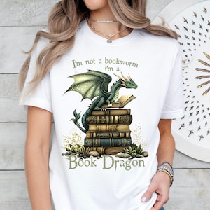 May include: White t-shirt with a green dragon sitting on a stack of books. The text on the shirt reads "I'm not a bookworm I'm a Book Dragon".