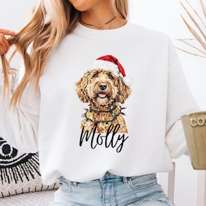 Pu&ograve; includere: Felpa bianca con un'illustrazione dettagliata di un cane con cappello di Babbo Natale e luci natalizie. Il nome del cane, "Molly", &egrave; scritto in un elegante script sottostante. La felpa &egrave; in stile casual.