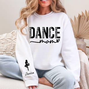 May include: White sweatshirt with the text "DANCE MOM" in black with a leopard print pattern. The sweatshirt has a black silhouette of a dancer on the left sleeve with the name "Jessica" underneath.
